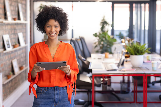 Young professional woman standing holding tablet in open-plan office, with floating shelves
