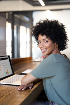Woman working on laptop at wooden counter in coworking space, with papers and pen, copy space