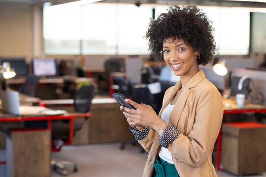 Professional woman standing and holding smartphone in brightly lit modern office, copy space