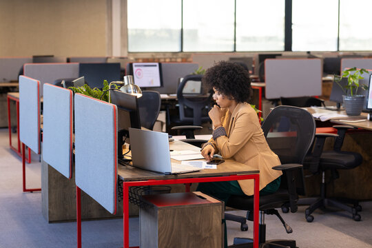 Woman reviewing paperwork at open-plan office desk with laptop smartphone and documents, copy space