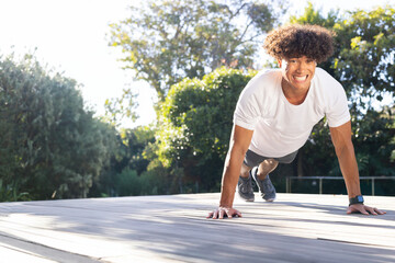 Man doing push ups on wooden deck in backyard, with fitness tracker, running shoes, copy space