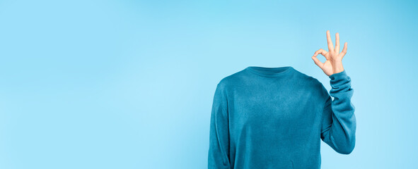 A headless individual dressed in a blue sweater makes a gesture of approval against a plain blue...
