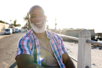 Senior African American man sitting on bench by metal railing on seaside walkway, enjoying sea view