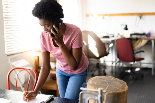 African American woman leaning over work table in creative studio, using pencil and sheets of paper