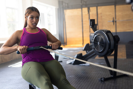 Woman using rowing machine in gym, showcasing focused workout and natural sunlight