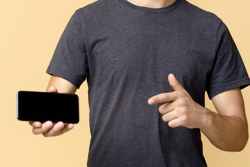Guy recommends, great offer, application or website for mobile device. Smiling young man in glasses points finger at smartphone with blank screen, isolated on light background, studio shot