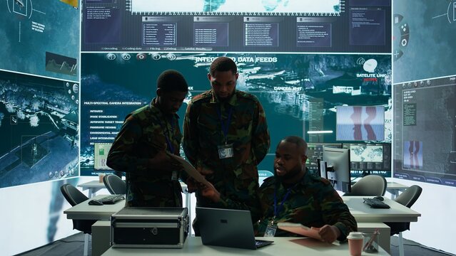 In a high tech military office, soldiers team analyze real time data collected by surveillance system. Staff interpret intelligence and coordinate operations to ensure national defense. Camera B.