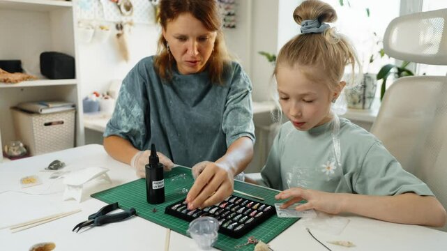Family crafting session filled with laughter and concentration as mother and daughter create unique resin pendants. Table covered with colorful materials enhances cozy atmosphere.