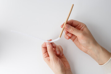 a step in a crafting process. It shows a pair of hands holding a paper pipe or straw with a white...