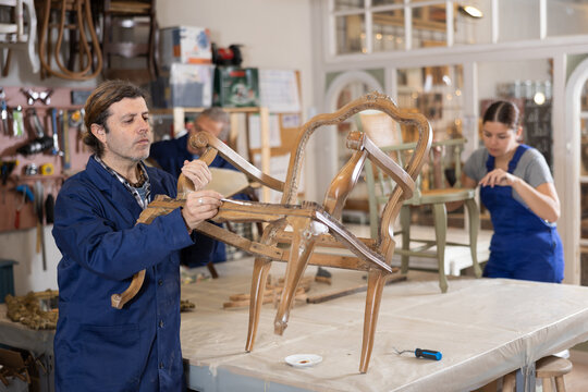 Male restorer restores the wooden frame of an antique chair