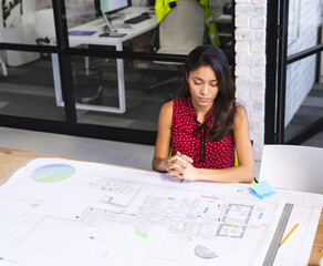 Young adult woman reviewing blueprints at design office, with yellow pencil and metal ruler