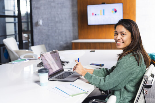 Woman marking printed charts with blue pen at conference table with laptop, copy space