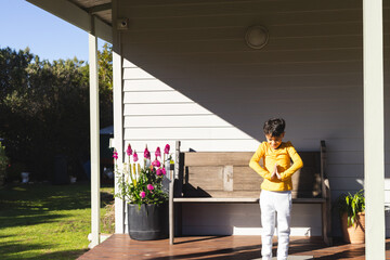 Young boy standing on front porch deck, clasping hands with planter of pink foxglove, copy space