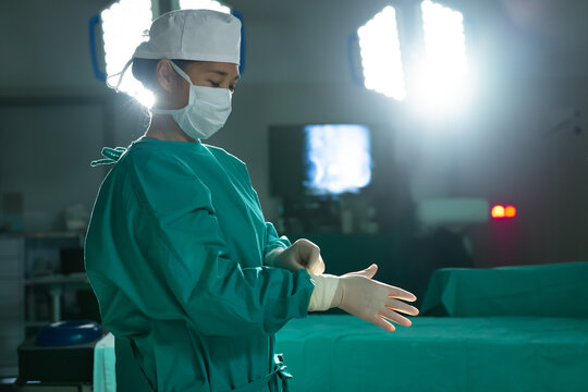Indian male surgeon donning sterile gloves in hospital operating room under LED lights, copy space