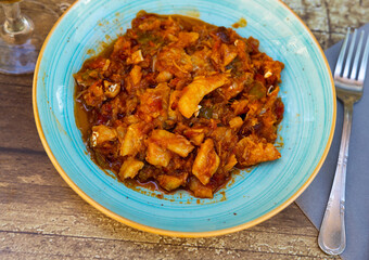 Cod stew with vegetables peppers, tomatoes, garlic and onions close-up in a bowl on the table