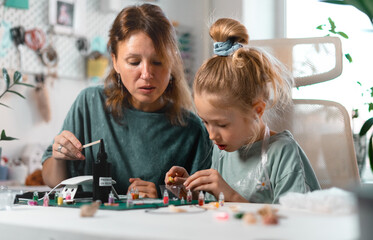 Fototapeta premium Engaging crafting experience where child immerses in handmade jewelry-making, carefully decorating resin pieces. Parent-child collaboration strengthens emotional connection.