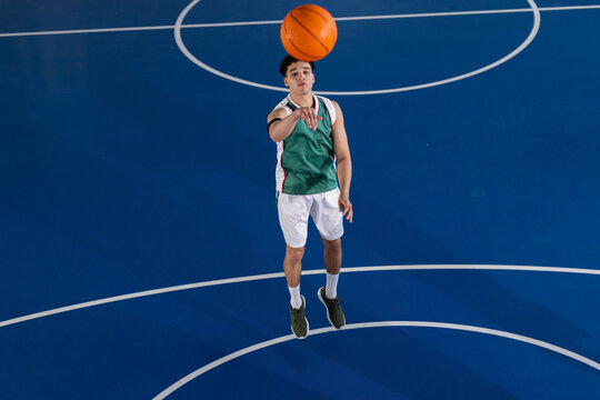 Man shooting orange basketball on deep blue basketball court, with white court markings