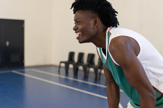 Teenage African American male athlete leaning on knees, smiling on basketball court, copy space