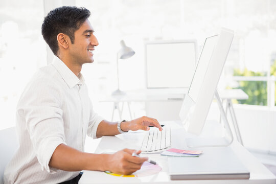 Indian man working at bright minimalist office desk with monitor and color swatches, copy space
