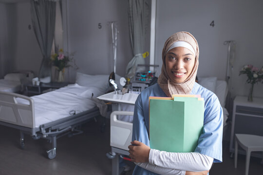 young adult woman wearing hijab sorting colored folders near IV pumps in hospital ward, copy space