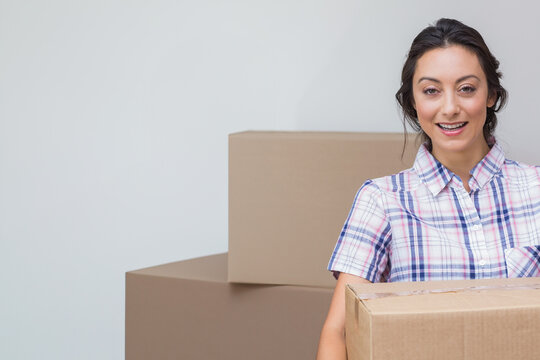 Mid-adult woman holding cardboard box in empty room at home, with stacked moving boxes