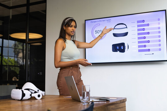 Woman presenting information in modern office meeting room, featuring VR headsets and laptop