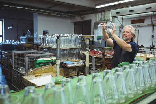 Senior man inspecting glass vessel in workshop, with beakers on green conveyor belt, copy space - Powered by Adobe