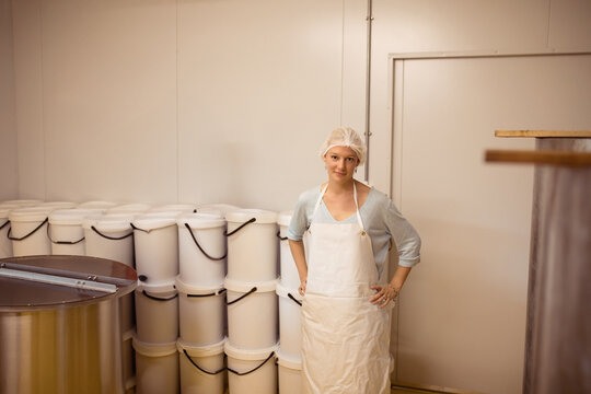 Woman wearing hairnet and apron operating vat in dairy plant room with stacked buckets, copy space