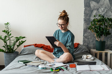 Young woman integrates technology into her study routine, working with digital and handwritten notes. Gadgets like wireless keyboard, tablet, and headphones make learning more engaging.