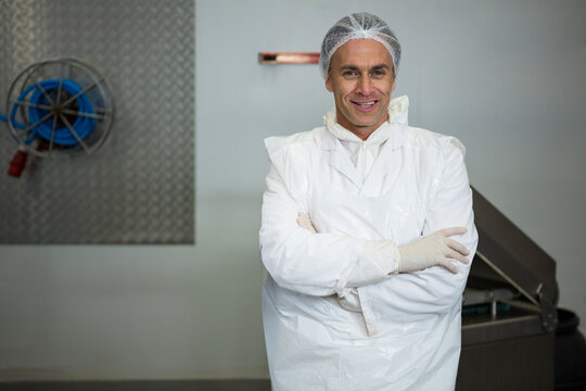 Mature male technician smiling in industrial plant, wearing lab coat, gloves at open hopper machine