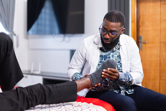 An African doctor examining an elderly patient's foot, skin and ankles during a home visit.