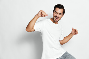Happy young man dancing wearing white t-shirt and grey pants isolated on plain gray background...