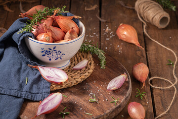A rustic kitchen with shallots in a bowl, fresh rosemary, a knife, and a blue cloth on a wooden cutting board, creating a cozy, homely atmosphere