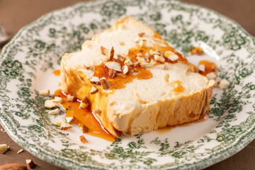 A close-up view features a slice of traditional caramelized egg white pudding known as molotof or molotov, generously drizzled with sweet syrup and sprinkled with almond pieces, on a decorative plate