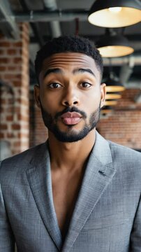 Young handsome African American man in a gray suit jacket making a kissy face expression indoors