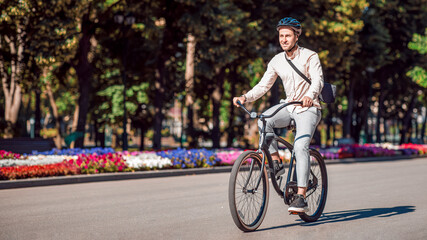 Urban eco transport. Handsome hipster in protective helmet enjoying bike riding in park, copy space