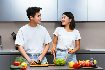 Cheerful Asian Couple Cooking Enjoying Dinner Preparation and Conversation Standing In Modern Kitchen At Home. Weekend Leisure, Healthy Food Recipes, Family Nutrition Concept