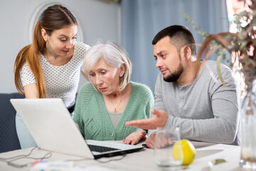 Young adult son and his wife giving help with laptop to stressed elderly mother at home