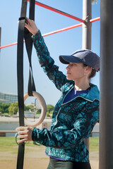 Female athlete preparing some gymnastic rings in an outdoor calisthenics park at sunny day.