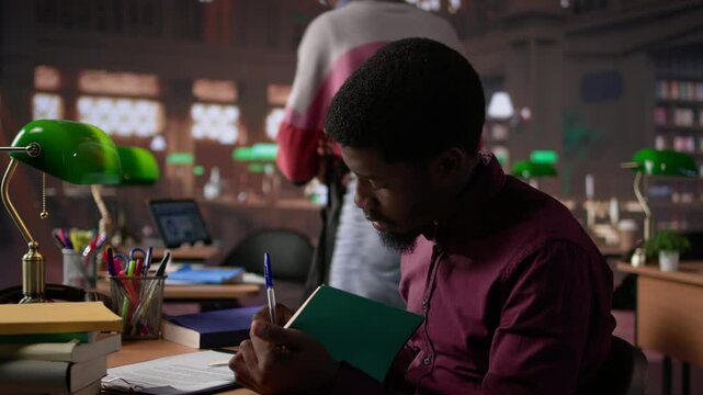 African american guy studies for a critical law exam and reading specialty books to complete class notes with reliable academic information. Studying in the library before the test. Camera B.