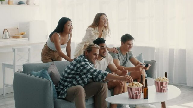 A group of five diverse friends is engaged in an exciting gaming session in a cozy living room. They are sharing laughter and snacks, demonstrating a relaxed and enjoyable atmosphere.