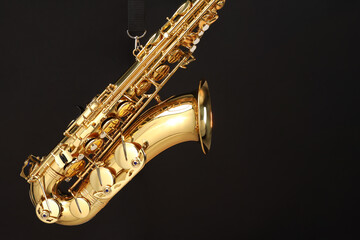 Jazz. One beautiful saxophone hanging from strap on black background, space for text