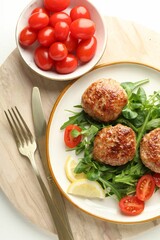 Delicious patties with greens, tomatoes and cutlery on white table, top view