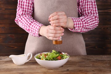 Woman salting tasty salad at wooden table, closeup