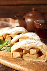 Pieces of tasty apple strudel with powdered sugar and mint on wooden table, closeup