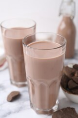 Tasty chocolate milk in glasses and pieces of chocolate on white marble table, closeup