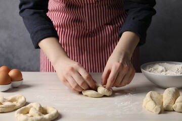 Woman making pretzel at white wooden table, closeup