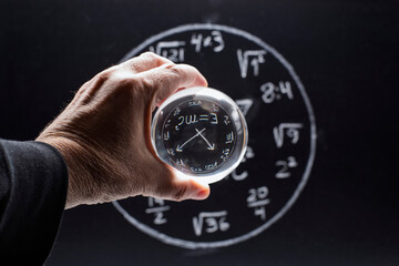 Mano con una bola de cristal delante de una pizarra con un reloj matemático dibujado con tiza