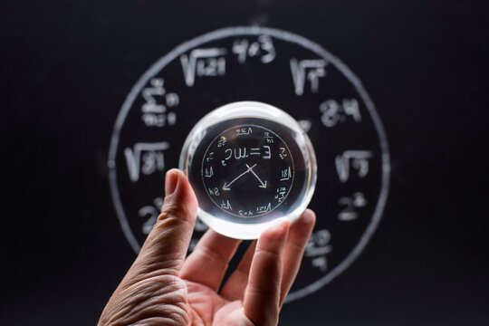 Mano con una bola de cristal delante de una pizarra con un reloj matemático dibujado con tiza