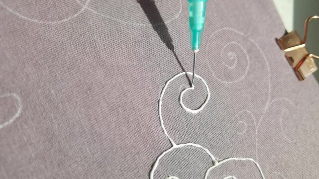 Closeup of embroidery process with turquoise tool stitching white threads on textured fabric.